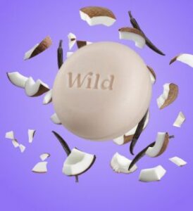 natural shampoo bar soap of beige color on lilac backgrownd with pieces of cocos and vanilla by wild cosmetics