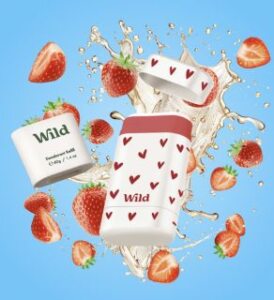 sustainable deodorant starter pack and reffil by the brand Wild Cosmetics with with cases on red small hearts all on blue background with cutted strawberries and splashes