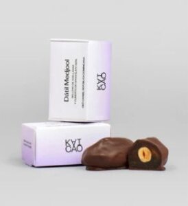 medjool dates filled with hazelnuts covered with 100% chocolate next to their box all on grey background