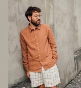 man with a coffe brown casual shoirt by matona and white shorts posing next to a grey wall presented by veganlyy.com