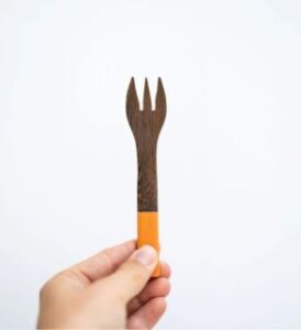 a handmade kids wooden fork in brown and orange in a hand presented by veganlyy.com