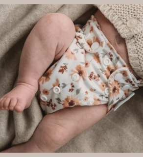 baby wearing one size all-in-one reusable sustainable cloth nappy benting leg on beige surface by veganlyy