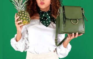 a woman holding pineapple leather green bag in one hand and pineapple in other presented by veganlyy