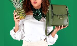 a woman holding pineapple leather green bag in one hand and pineapple in other presented by veganlyy