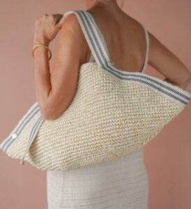 veganlyy stelar penge raffia shoulder beach bag with black and cream stripes worn over a tanned woman's shoulder
