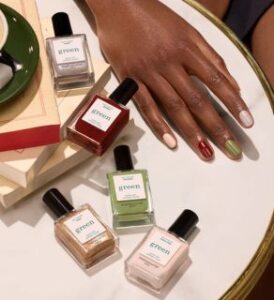 5 natural green vegan polish from manicurist veganlyy rainbow collections with black lady's hand on white table cover