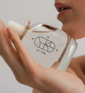 veganlyy young woman holding a wa:it eau de perfume with her right hand and touching with the flask her chin